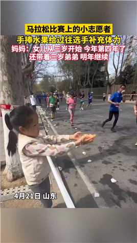 马拉松比赛上的小志愿者 手捧水果给过往选手补充体力，妈妈：女儿从三岁开始 今年第四年了，还带着三岁弟弟 明年继续