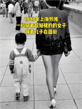 这是1993年上海外滩，一位穿着超短裙的女子，领着儿子在逛街。那时候人们的穿着还很保守，女子穿着超短裙是非常时尚的，孩子的穿着也不错，可见他们家境不错！