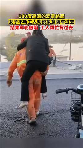 180度高温的沥青路面，女子不听工人劝说执意骑车过去。结果车轮被陷，工人帮忙背过去。