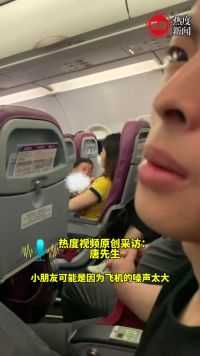 飞机上一男孩在妈妈怀里哭闹，隔壁男子用喝水动作哄他。