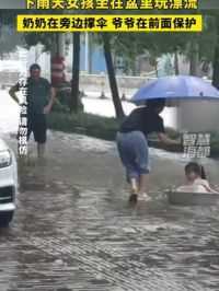 下雨天女孩坐在盆里玩漂流，奶奶在旁边撑伞，爷爷在前面保护
