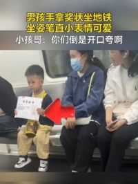 男孩手拿奖状坐地铁，坐姿笔直小表情可爱（来源：人民网）