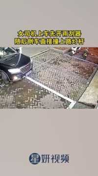 女司机上车先开雨刮器，随后倒车直接撞上路灯杆。